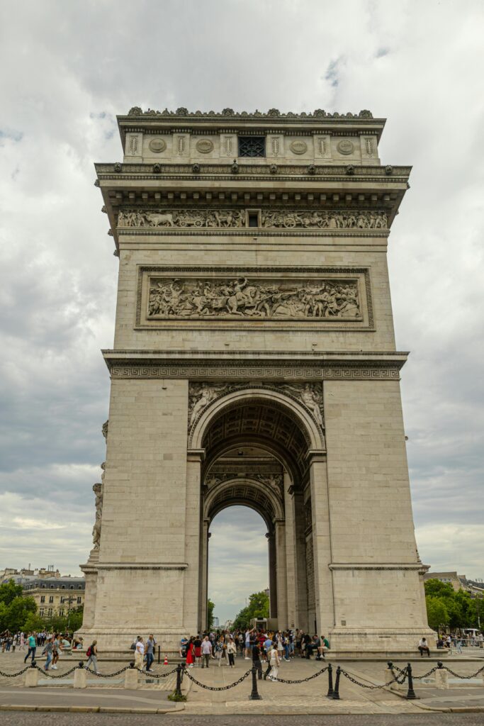A view of the iconic Arc de Triomphe in Paris with a cloudy sky backdrop.